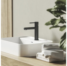 Čierna matná umývadlová batéria na bielom umývadle na dosku na drevenom podklade v kúpeľni s uterákmi.