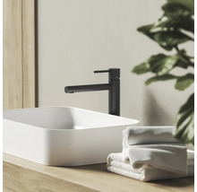 Moderná kúpeľňová scéna s čiernou pákovou umývadlovou batériou a bielym umývadlom na dosku na drevenom podklade s uterákmi.