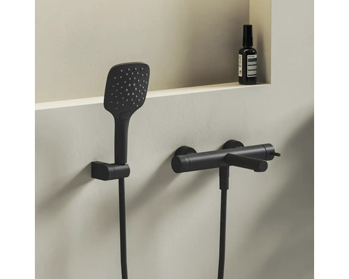 Moderný sprchový set v matnej čiernej farbe s obdĺžnikovou ručnou sprchou a valcovou nástennou batériou v minimalistickej kúpeľni.