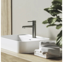 Umývadlová batéria vo vzhľade nehrdzavejúcej ocele na bielom umývadle na dosku, s drevenou doskou a bielymi uterákmi.