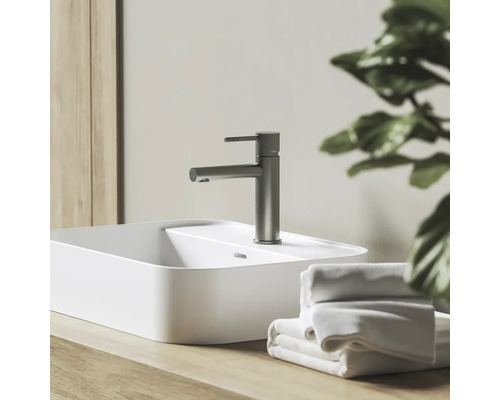 Umývadlová batéria vo vzhľade nehrdzavejúcej ocele na bielom umývadle na dosku, s drevenou doskou a bielymi uterákmi.