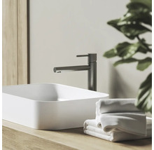 Moderná kúpeľňa s bielym umývadlom na dosku, tmavosivou batériou na drevenej doske a bielymi uterákmi.