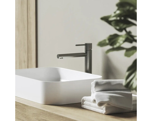 Moderná kúpeľňa s bielym umývadlom na dosku, tmavosivou batériou na drevenej doske a bielymi uterákmi.