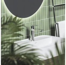 Moderná kúpeľňa s bielym umývadlom, chrómovou batériou, zelenými vertikálnymi obkladmi a okrúhlym zrkadlom.