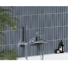 Moderná nástenná vaňová batéria s ručnou sprchou v chróme na stene s tmavomodrými zvislými obkladmi.