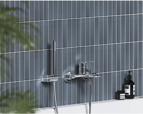 Moderná nástenná vaňová batéria s ručnou sprchou v chróme na stene s tmavomodrými zvislými obkladmi.
