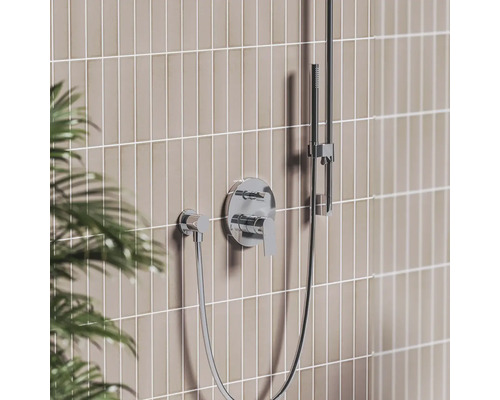 Moderná podomietková sprchová batéria v chróme s pákovým ovládaním, nástennou prípojkou a ručnou sprchou na tyči pred obloženou stenou.