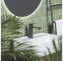 Čierna matná umývadlová batéria na bielom umývadle pred zelenou obloženou stenou s okrúhlym zrkadlom a držiakom na uteráky v modernej kúpeľni.