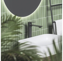 Čierna umývadlová batéria pri bielom umývadle na dosku pred zelenými obkladmi s osvetleným zrkadlom v modernej kúpeľni.