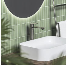 Moderná kúpeľňa s bielym umývadlom na dosku, vysokou tmavou batériou a zeleným vertikálnym obkladom.