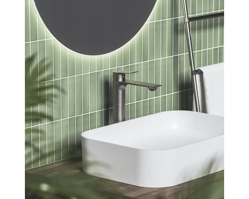 Moderná kúpeľňa s bielym umývadlom na dosku, vysokou tmavou batériou a zeleným vertikálnym obkladom.