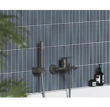 Nástenná vaňová batéria s ručnou sprchou v tmavom kovovom vyhotovení na vertikálne obloženej stene.