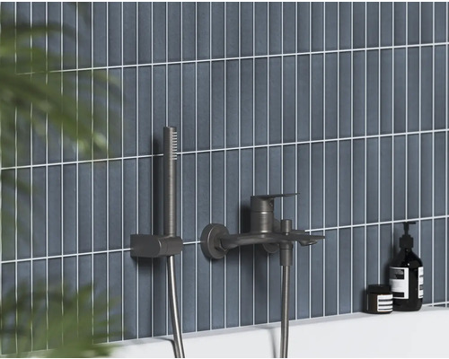 Nástenná vaňová batéria s ručnou sprchou v tmavom kovovom vyhotovení na vertikálne obloženej stene.