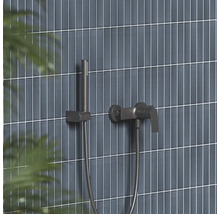 Moderná sprchová batéria a tyčová ručná sprcha v tmavom kovovom vzhľade na stene s úzkymi vertikálnymi obkladmi.