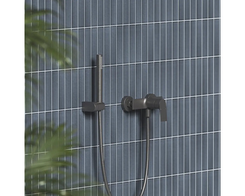 Moderná sprchová batéria a tyčová ručná sprcha v tmavom kovovom vzhľade na stene s úzkymi vertikálnymi obkladmi.