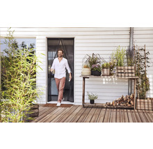 Muž prechádza cez magnetický záves proti hmyzu na terasových dverách na drevenú terasu s mnohými rastlinami v kvetináčoch.