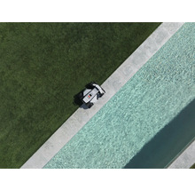 Robotická kosačka na okraji trávnika vedľa bazéna s kamenným lemom, pohľad zhora.