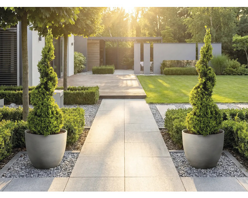 Moderná svetlá záhrada s kamenným chodníkom, špirálovito tvarovanými drevinami v okrúhlych kvetináčoch, drevenou terasou a trávnikom.