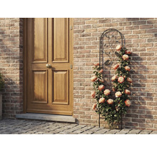 Kovová mriežka na popínavé rastliny s motívom vtákov a listov, s popínavými ružami pri tehlovej stene vedľa drevených dverí.