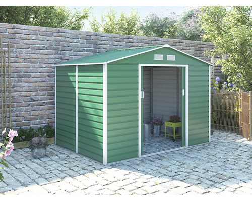 Zelený kovový záhradný domček so sedlovou strechou a posuvnými dverami na dláždenej terase pri tehlovom múre.