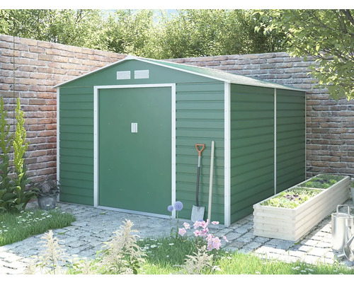 Zelený kovový záhradný domček so sedlovou strechou a bielym rámom v záhrade pred tehlovou stenou.