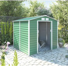 Zelený kovový záhradný domček so sedlovou strechou a bielym rámom, posuvnými dverami a ventiláciou, na kamennej dlažbe vo svetlej záhrade.