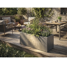 Veľký obdĺžnikový kvetináč v betónovom vzhľade na drevenej terase v moderne navrhnutej záhrade s posedením a ohniskom.