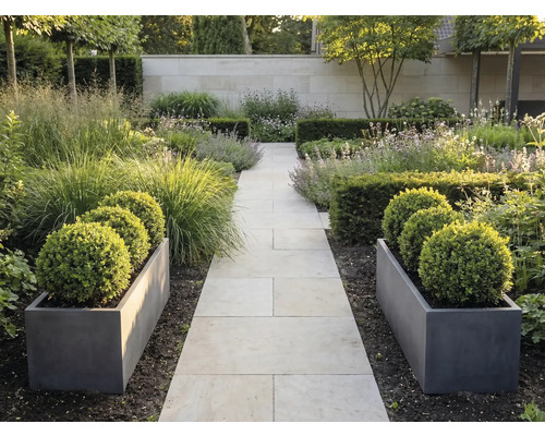 Moderná záhrada so svetlou kamennou cestou, sivými kvetináčmi s buxusovými guľami a okrasnými trávami pri múre.