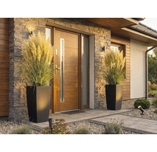 Moderný vchod do domu s drevenými dverami, kamenným obkladom a dvoma vysokými kvetináčmi v ratanovom vzhľade s pampovou trávou.