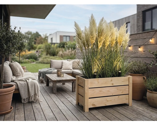 Moderná drevená terasa s veľkým kvetináčom s pampovou trávou, vonkajším nábytkom s vankúšmi, stolíkom a dekoratívnym osvetlením.