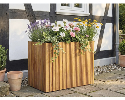 Veľký obdĺžnikový kvetináč z drevených latiek, vysadený levanduľou a pelargóniami, na terase pred hrazdenou fasádou.