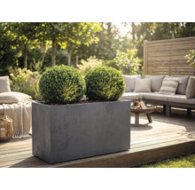 Obdĺžnikový sivý kvetináč s dvoma guľovitými krušpánmi na drevenej terase v záhradnom salóniku s ohniskom a pohovkou.