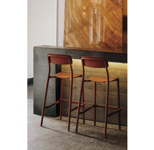 Dve moderné barové stoličky v terakotovej farbe pri betónovom pulte, dekoratívny panel so vzhľadom dreva, atmosférické osvetlenie.