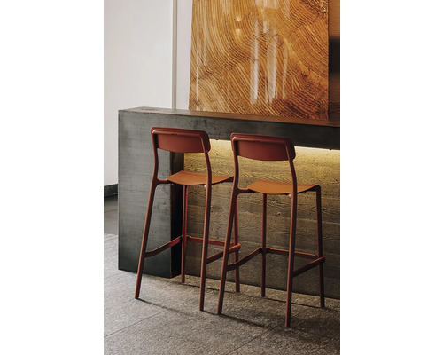 Dve moderné barové stoličky v terakotovej farbe pri betónovom pulte, dekoratívny panel so vzhľadom dreva, atmosférické osvetlenie.