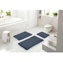 Svetlá moderná kúpeľňa s tromi modrými štruktúrovanými kúpeľňovými predložkami na bielej dlažbe, vrátane vane, toalety a umývadla.