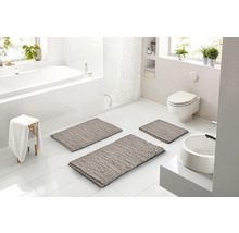 Svetlá, moderná kúpeľňa s tromi sivými kúpeľňovými predložkami na bielej dlažbe, vaňou, toaletou a umývadlom v bielej farbe.