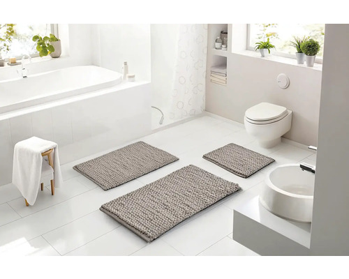 Svetlá, moderná kúpeľňa s tromi sivými kúpeľňovými predložkami na bielej dlažbe, vaňou, toaletou a umývadlom v bielej farbe.