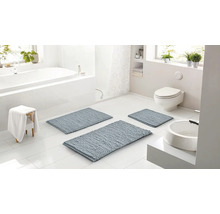 Svetlá kúpeľňa s tromi modrosivými kúpeľňovými predložkami rôznych veľkostí, bielou vaňou, toaletou a umývadlom.