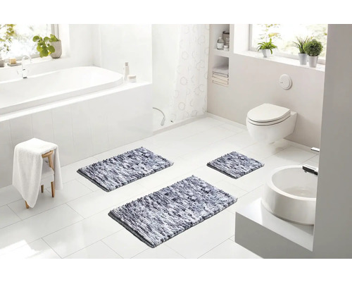 Svetlá moderná kúpeľňa s bielou vaňou, toaletou a tromi sivými melírovanými kúpeľňovými predložkami na bielej dlažbe.