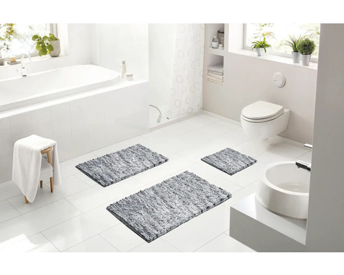 Svetlá moderná kúpeľňa s bielou vaňou, závesnou toaletou, umývadlom a tromi sivými kúpeľňovými predložkami na podlahe.