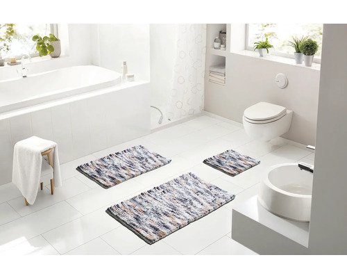 Svetlá kúpeľňa s vaňou, toaletou a umývadlom, vybavená tromi viacfarebnými kúpeľňovými predložkami rôznych veľkostí.