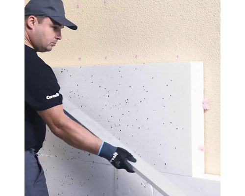 Remeselník inštaluje polystyrénovú izolačnú dosku na fasádu budovy počas zatepľovania.