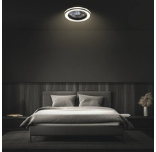 Moderný stropný ventilátor s LED osvetlením v tmavo zariadenej spálni nad sivou čalúnenou posteľou.
