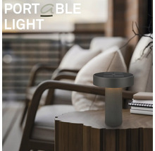 Moderná prenosná stolná LED lampa na drevenom stole vo vonkajšom priestore s kreslami.