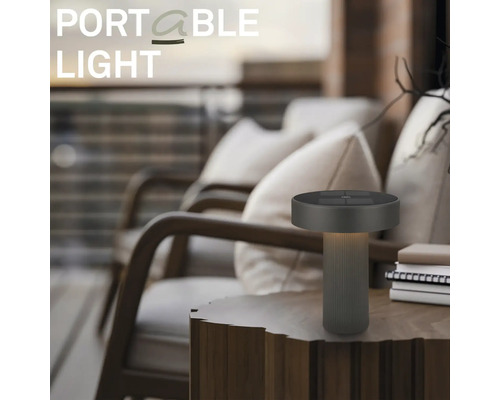 Moderná prenosná stolná LED lampa na drevenom stole vo vonkajšom priestore s kreslami.