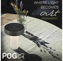 Solárna stolná lampa Poga s drážkovaným podstavcom na prestretom záhradnom stole vedľa vázy s kvetmi.
