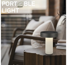 Prenosná stolná LED lampa na drevenom stole v modernom vonkajšom priestore s pohodlnými kreslami.
