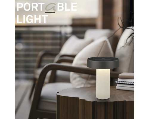 Prenosná stolná LED lampa na drevenom stole v modernom vonkajšom priestore s pohodlnými kreslami.