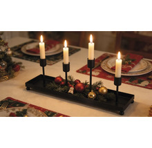 Adventný svietnik z čierneho kovu so štyrmi držiakmi na sviečky, zdobený jedľovou čečinou a vianočnými guľami na slávnostne prestretom stole.