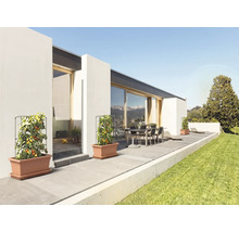 Rajčiaky v plastových kvetináčoch s mriežkami na modernej terase so záhradným nábytkom a priľahlým trávnikom.